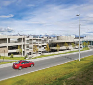 Red car passing a multi-level parking garage
